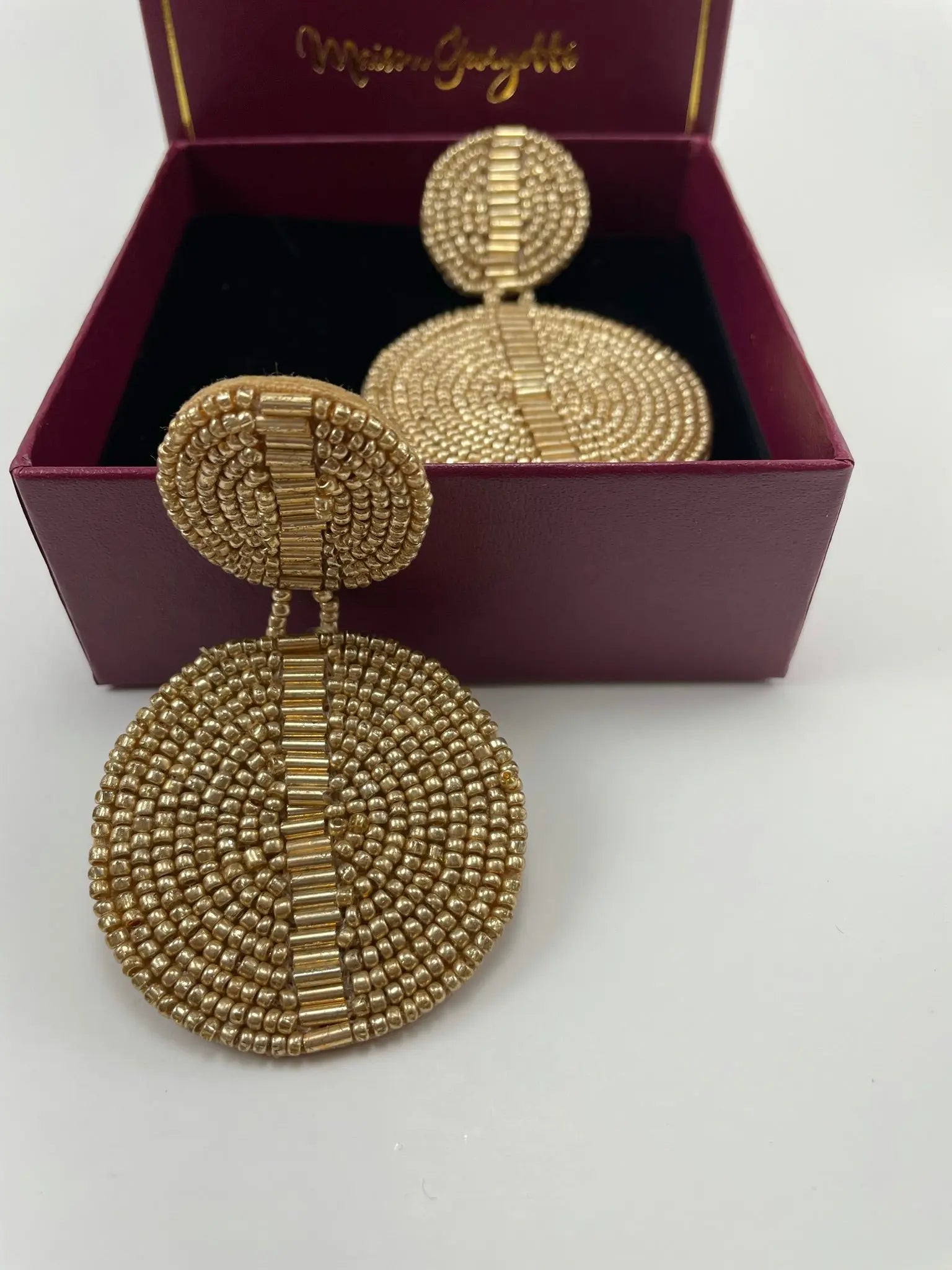 A box containing gold beaded earrings, representing the affordable luxury of the Brenda Discus Earring line