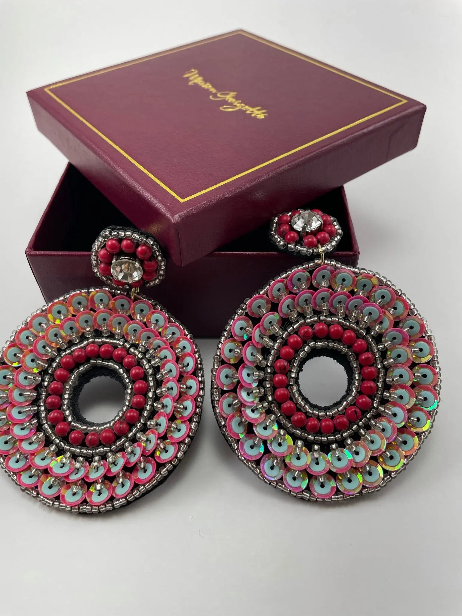 A pair of red and black Evie Red Sequin Hoop earrings displayed in a box, showcasing statement jewelry.