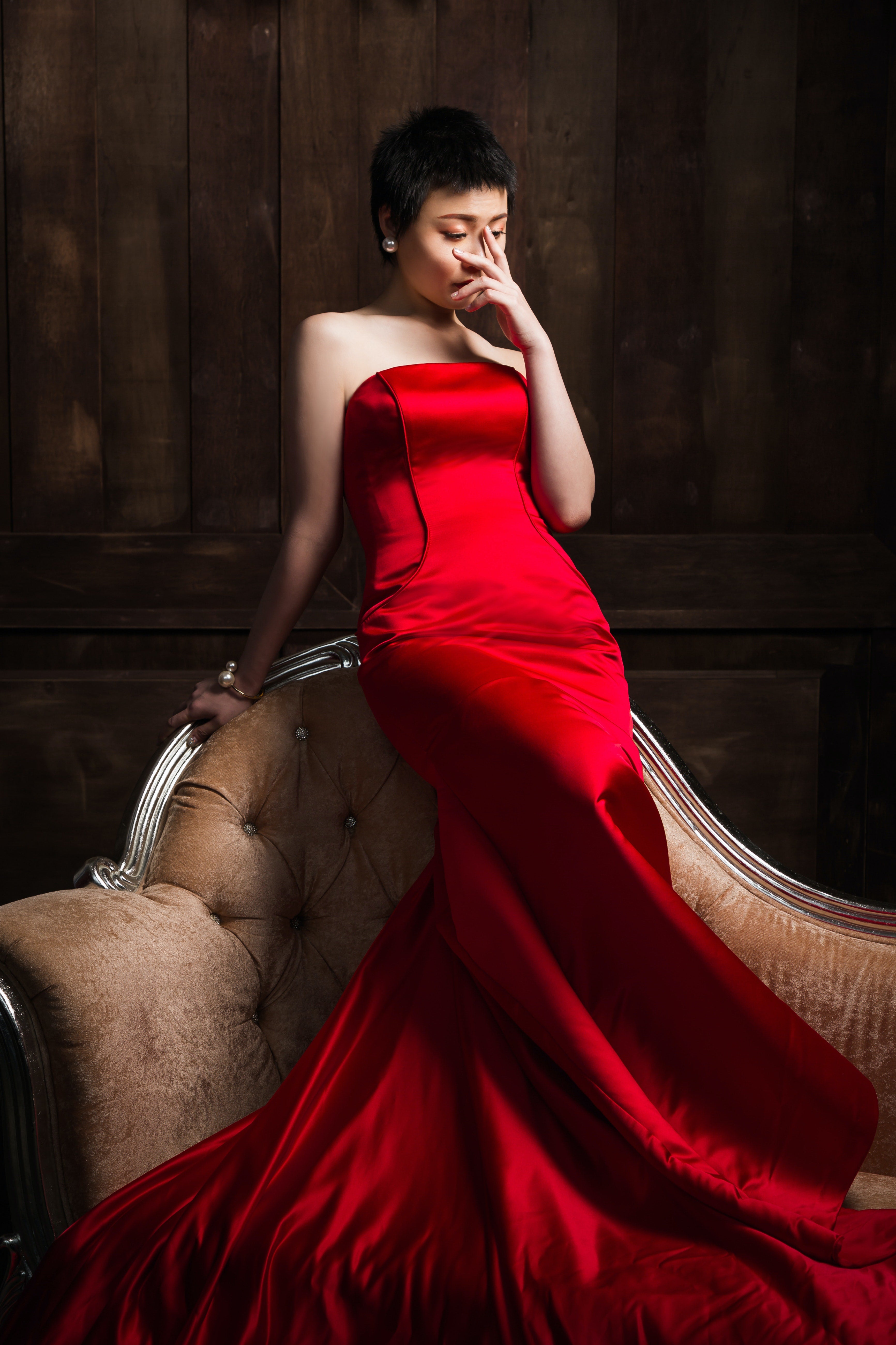 A woman in a red dress poses on a chair, accentuating her stylish affordable luxury jewelry.