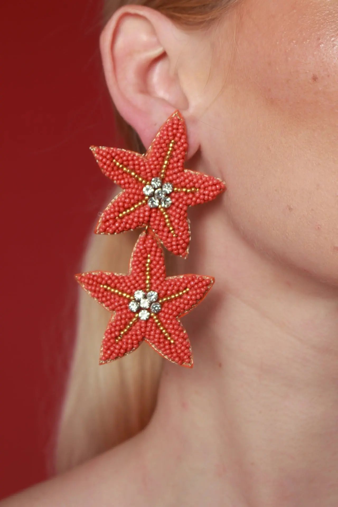 A woman showcases a Sea Star earring, featuring a striking red flower design, embodying timeless jewelry